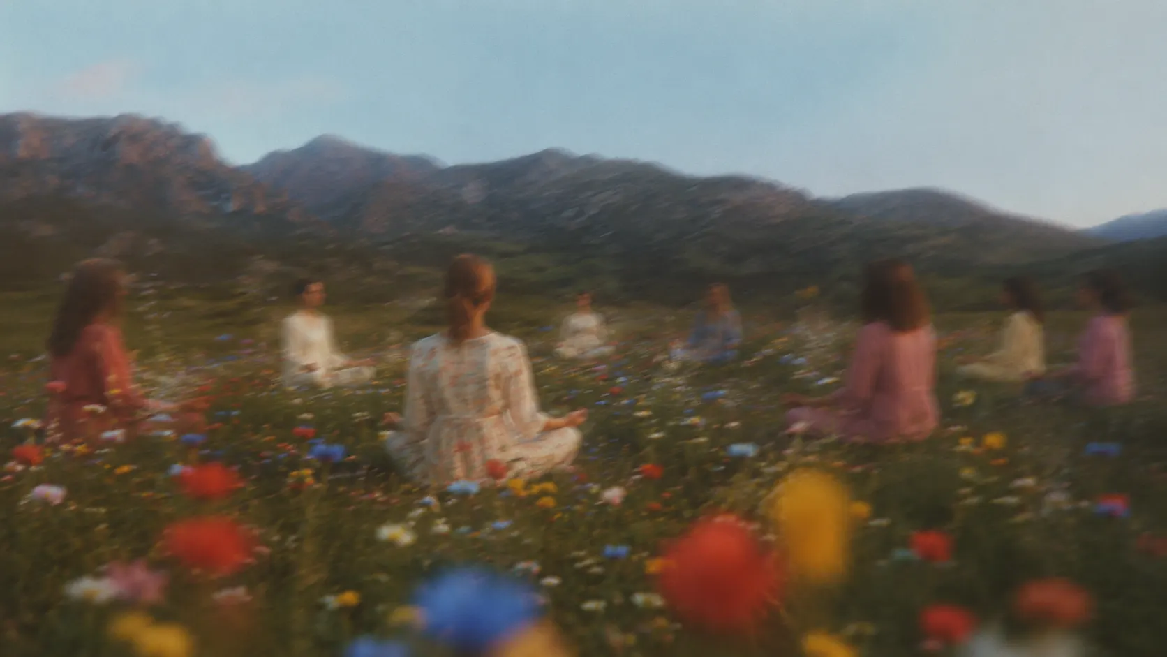 people meditating in a wildflower meadow beneath mountains at dusk